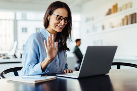 Woman waving on a video call while sitting in an office. Female designer having an online meeting with her business clients on a laptop.